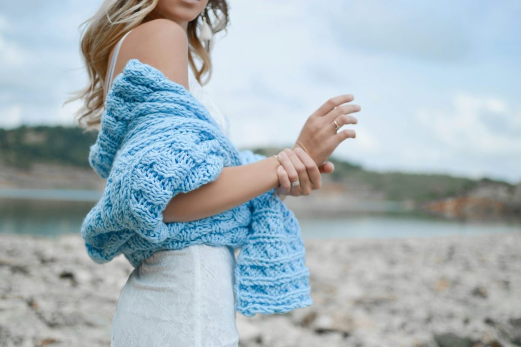 Femme portant un haut en crochet bleu sarcelle et une jupe blanche.